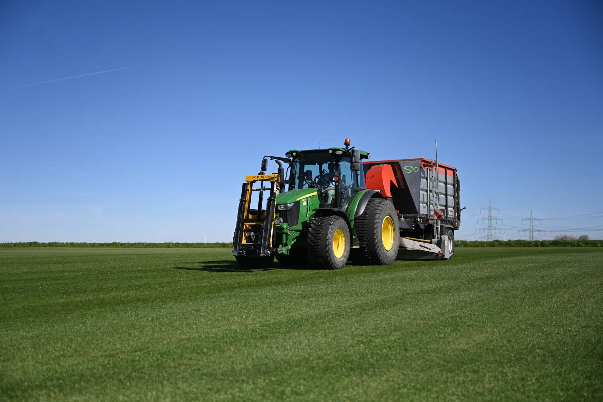 Traktor mit Aufsammelwagen saugt das Schnittgut vom Feld ab