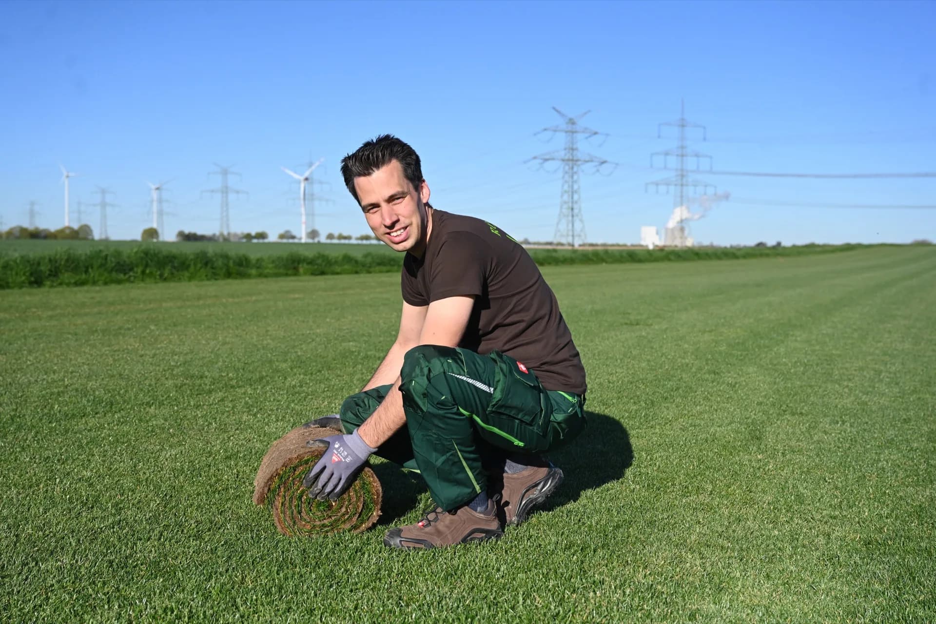 Thomas Decker mit einer frischen Rolle Premium Sport Rollrasen vor sattgrüner Rasenfläche